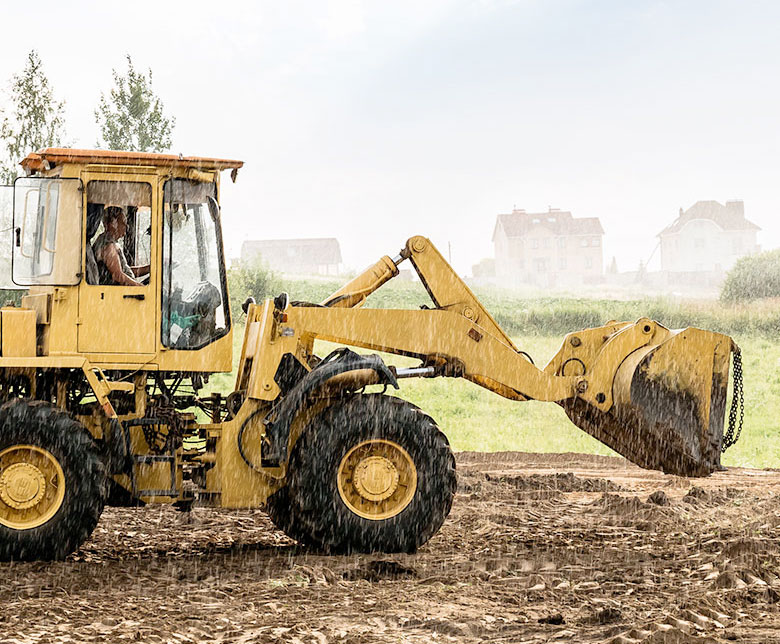 Yellow construction machinery picking up dirt land in the rain tomlin investments land investing in texas